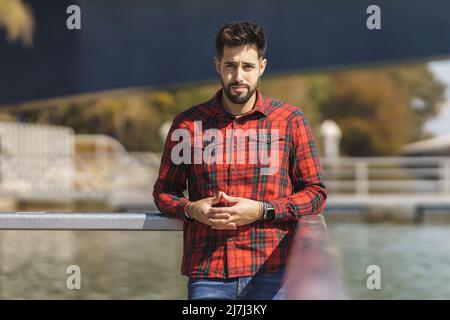 gay aux cheveux sombres avec barbe et chemise rouge regardant l'appareil photo Banque D'Images