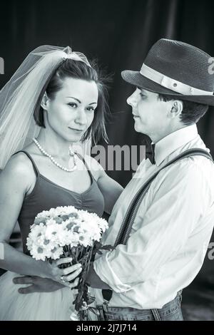 Portrait d'un jeune couple en tenue de mariage célébrant leur anniversaire de mariage en noir et blanc. Sourire, baiser, tenir le bouquet ensemble, l'amour Banque D'Images