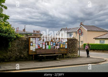 06.05.2022 Settle, North Yorkshire, Royaume-Uni installez un panneau d'affichage communautaire avec une banquette marron en dessous et une femme avec un sac rose Banque D'Images