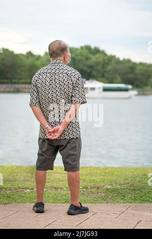 Vue arrière d'un homme asiatique senior qui regarde à l'horizon d'un lac. Concept de voyage ou de vacances. Banque D'Images