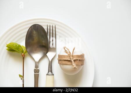 Le couteau, la fourchette et la cuillère se trouvent dans une assiette blanche sur fond blanc, et à côté se trouve une branche d'arbre avec des feuilles vertes, la mise en table, le bu de restaurant Banque D'Images