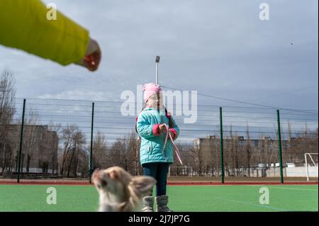 Une famille avec un animal de compagnie sur l'aire de jeux. La jeune fille de cinq ans à l'arrière-plan est debout tenant la laisse du chien. La main de maman tient une friandise sur elle Banque D'Images