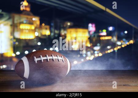 Ballon de rugby sur une table en bois contre une ville nocturne floue Banque D'Images