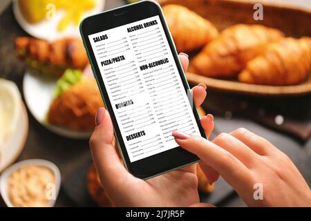 Jeune femme lisant le menu sur l'écran du téléphone mobile, gros plan Banque D'Images