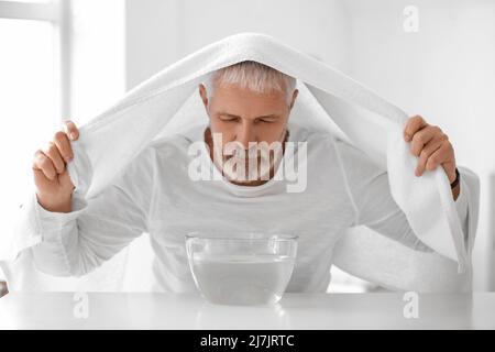 Homme mûr avec une serviette faisant inhalation de vapeur à la maison Banque D'Images