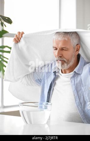Homme mûr avec une serviette faisant inhalation de vapeur à la maison Banque D'Images
