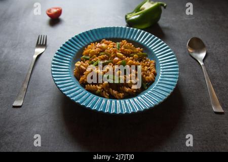 Pâtes en spirale de légumes servies dans un bol bleu sur fond sombre. Vue de dessus, mise au point sélective. Banque D'Images