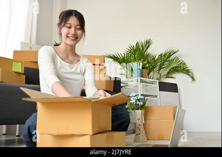 Une jeune femme asiatique attirante l'empaquit dans des boîtes en carton, préparant le colis pour le déménagement ou le déménagement dans une nouvelle maison. Banque D'Images