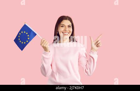 Femme caucasienne portant un petit drapeau avec emblème de l'Union européenne isolée sur fond rose. Banque D'Images