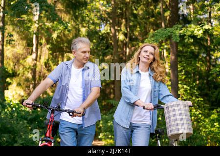 Vieux âge actif, gens et style de vie concept heureux couple senior fixant le vélo, parlant sur le parc de la ville d'été sur le chemin dans la forêt ensoleillée, portant des vêtements décontractés mignon homme et femme caucasien Banque D'Images