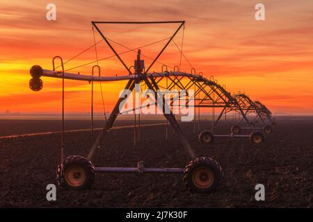 Déplacement latéral système d'irrigation agricole sur le champ labouré au coucher du soleil, équipement agricole pour l'arrosage des terres agricoles cultivées Banque D'Images