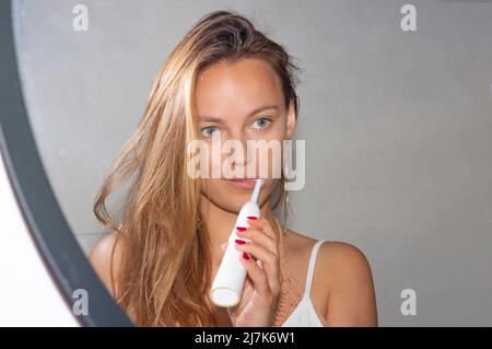 jolie femme blonde se brossant les dents avec une brosse à dents électrique Banque D'Images