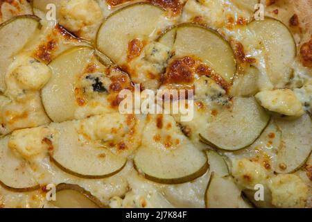 Pizza en tranches avec poire, gorgonzola et miel en nid d'abeille sur papier à pâtisserie vue de dessus, gros plan. Banque D'Images