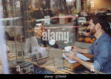 Conversation gaie de jeunes amis ou partenaires d'affaires de races mixtes. Pause café au café. Banque D'Images