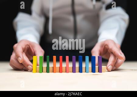 Photo conceptuelle des mains préparant une rangée de pierres domino. Effet Domino avec pierres colorées et espace de copie Banque D'Images