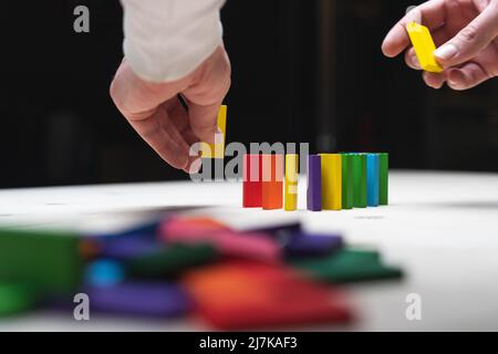 Photo conceptuelle des mains préparant une rangée de pierres domino. Effet Domino avec pierres colorées et espace de copie Banque D'Images