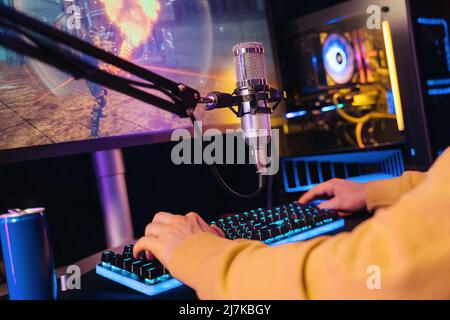 Gros plan sur les mains des gamers professionnels qui se posent sur le clavier de jeu pendant qu'il diffuse son jeu vidéo en ligne sur un PC puissant à la maison. Configuration professionnelle pour les tournois de cybersport et les jeux. Couleur néon Banque D'Images