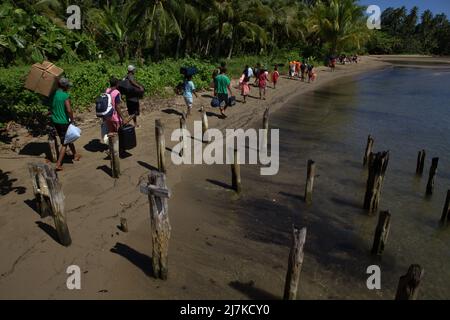 Les villageois portent les bagages des touristes arrivant par bateau, alors qu'ils marchent le long de la plage dans le village de Horale, île de Seram, Maluku central, Maluku, Indonésie. Banque D'Images