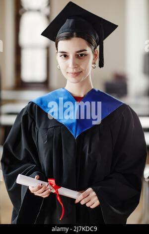 Portrait vertical de la jeune femme portant une robe de graduation et souriant à l'appareil photo Banque D'Images