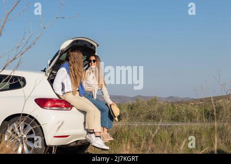 Amis assis dans une chaussure de voiture blanche, prenant une pause de la conduite pendant un voyage de printemps sur route. Dans un paysage vert sous ciel bleu et espace de copie Banque D'Images