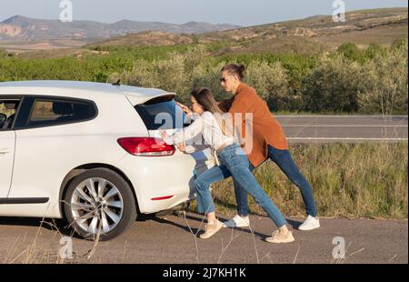 Homme et femme poussant une voiture blanche brisée, vue arrière. Au milieu de nulle part dans la campagne au printemps Banque D'Images