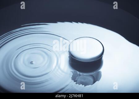 Image minimaliste d'un verre d'eau dont la goutte tombe à la surface de l'eau. Image abstraite de l'eau en bleu monochrome. Banque D'Images