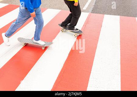 Vue rognée de deux amis sans visage patineurs portant des chandails bleus et jaunes patinage par une traversée de zèbre Banque D'Images