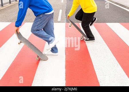 Vue rognée de deux amis sans visage patineurs portant des chandails bleus et jaunes patinage par une traversée de zèbre Banque D'Images