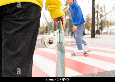 Vue rognée de deux amis sans visage patineurs portant des chandails bleus et jaunes patinage par une traversée de zèbre Banque D'Images