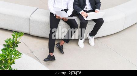 Par le dessus, des collègues masculins multiraciaux non reconnaissables sont coupés en tenue habillée avec des documents dactylographiés sur un netbook moderne tout en travaillant ensemble sur un projet Banque D'Images