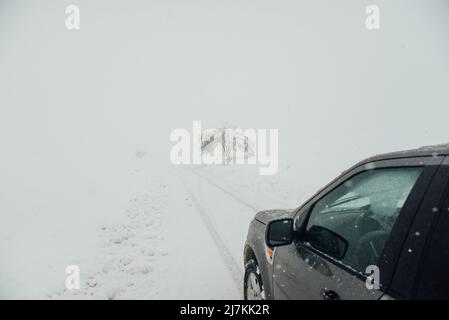 Automobile moderne conduite sur route vide recouverte de neige par temps froid en hiver dans la campagne par temps brumeux Banque D'Images