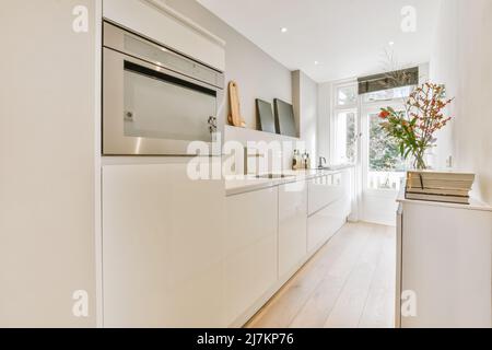 Vase avec bouquet de fleurs placé sur le comptoir de cuisine avec placards blancs et appareils modernes dans une cuisine élégante avec fenêtre Banque D'Images