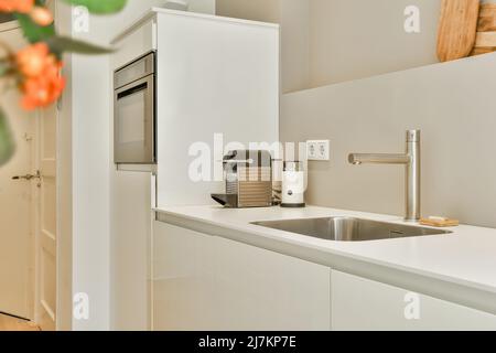 Vase avec bouquet de fleurs placé sur le comptoir de cuisine avec placards blancs et appareils modernes dans une cuisine élégante avec fenêtre Banque D'Images