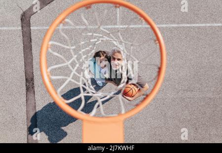 Père heureux et fille de l'adolescence embrassant et se tenant sous un filet de basket-ball, directement au-dessus Banque D'Images