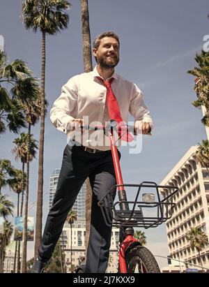 Un homme d'affaires heureux a plaisir à se faire une petite arnaque le long de la rue de la ville, e-scooter Banque D'Images