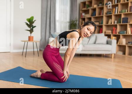 Femme coréenne pratiquant le yoga uddiyana bandha exercice de verrouillage abdominal tout en étant assise sur le tapis de yoga à la maison Banque D'Images
