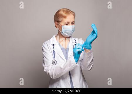 Concept médical de la femme mature médecin en manteau blanc avec stéthoscope mettant des gants médicaux Banque D'Images