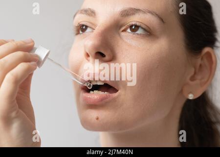 Portrait de la jeune femme aux cheveux foncés prenant un supplément d'huile avec un compte-gouttes en verre. CBD huile de médecine de chanvre appliquée sur la langue Banque D'Images