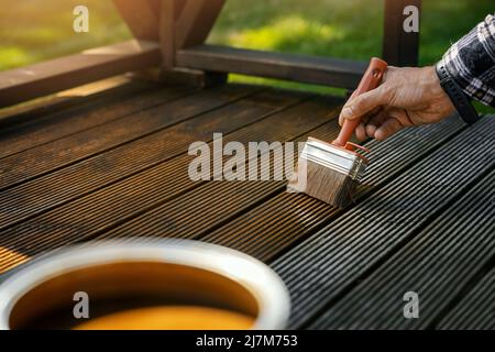 homme appliquant de l'huile de protection en bois brun sur les lames de terrasse avec un pinceau. rénovation de la terrasse Banque D'Images