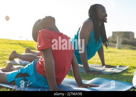 Père et fils afro-américains pratiquant le yoga flexible sur des tapis le matin Banque D'Images