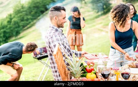 Les jeunes amis s'amusent sur le pique-nique en plein air pour préparer la nourriture au barbecue - des gens heureux cuisinant et mangeant dans un restaurant en plein air de campagne Banque D'Images