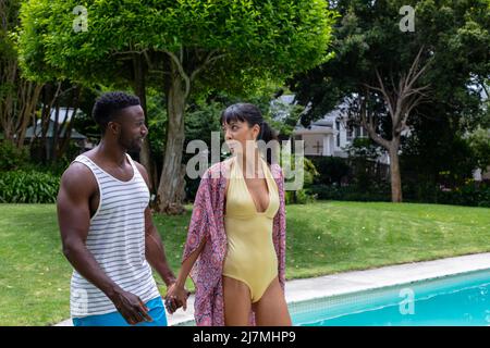 Jeune couple multiracial marchant au bord de la piscine dans l'arrière-cour. Non modifié, ensemble, style de vie, loisirs, collage, activités le week-end. Banque D'Images