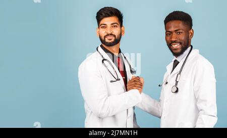 portrait d'un professionnel de santé souriant en blouse de laboratoire blanche avec stéthoscope conférant avec un jeune médecin sur fond bleu Banque D'Images