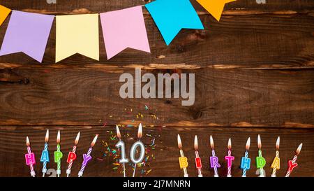 Vue de dessus, décorations d'anniversaire de lettres de bougie avec feu et guirlandes de vacances, espace de copie. Fond joyeux anniversaire avec numéro sur table brune. Banque D'Images