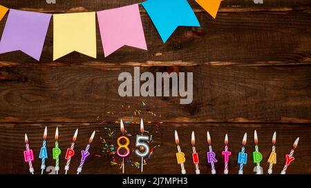 Vue de dessus, décorations d'anniversaire de lettres de bougie avec feu et guirlandes de vacances, espace de copie. Fond joyeux anniversaire avec numéro sur table brune. Banque D'Images