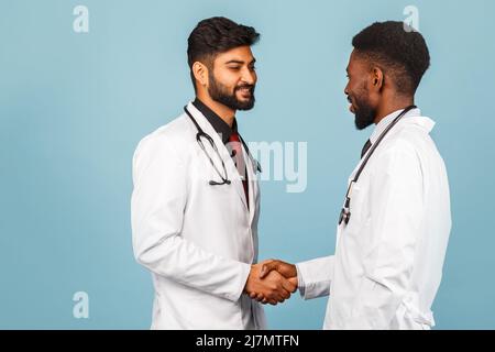 portrait de przloseup d'un professionnel de la santé intellectuel avec un laque blanc discutant des résultats avec un jeune médecin sur fond bleu Banque D'Images