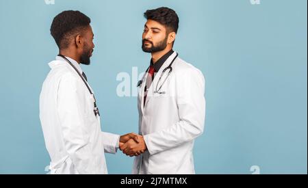 portrait de przloseup d'un professionnel de la santé intellectuel avec un laque blanc discutant des résultats avec un jeune médecin sur fond bleu Banque D'Images