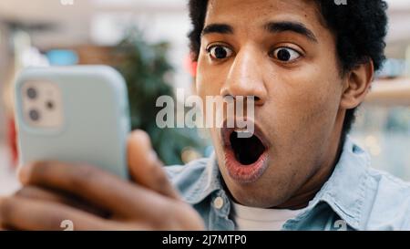 Un gars afro-américain surpris par le message reçu gagne des Paris en ligne regarder le téléphone mobile ouvre la bouche dans surprise enchantée de choc homme se sent Banque D'Images