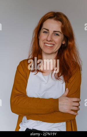 Bonne femme d'âge moyen au gingembre dans son 40s sur le mur blanc. Employé dans une tenue décontractée regardant l'appareil photo. Femme aux cheveux longs, gaie Banque D'Images