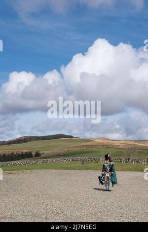 Un bagpiper mâle plus âgé portant un tartan bleu et vert traditionnel spécifique à un clan écossais particulier, tout en tenant un bagpipe et debout composé Banque D'Images